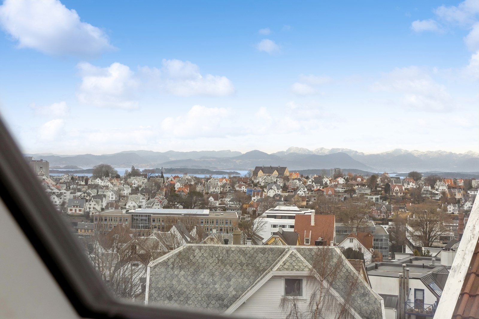 Utsikt over hustak fra et vindu med fjell i horisonten. Galleribilde