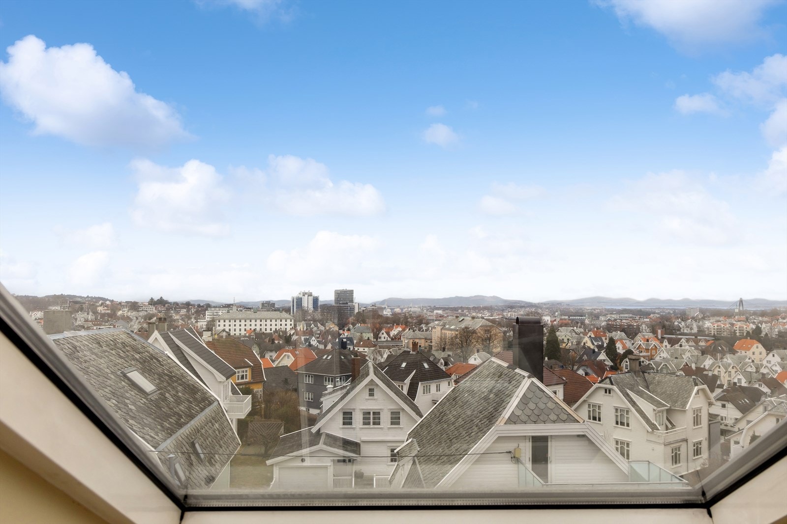 Utsikt over bylandskap fra et vindu med fjell i bakgrunnen. Galleribilde