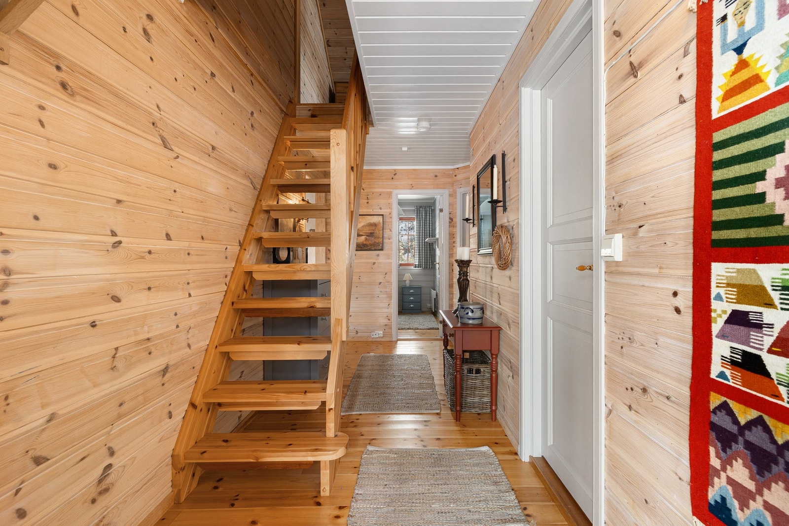 Entréen gir et hyggelig førsteinntrykk med gjennomgående furugulv og panelte vegger som viderefører den lune hytteatmosfæren. Her er det adkomst til hyttens øvrige rom, samt trapp opp til hems. Galleribilde
