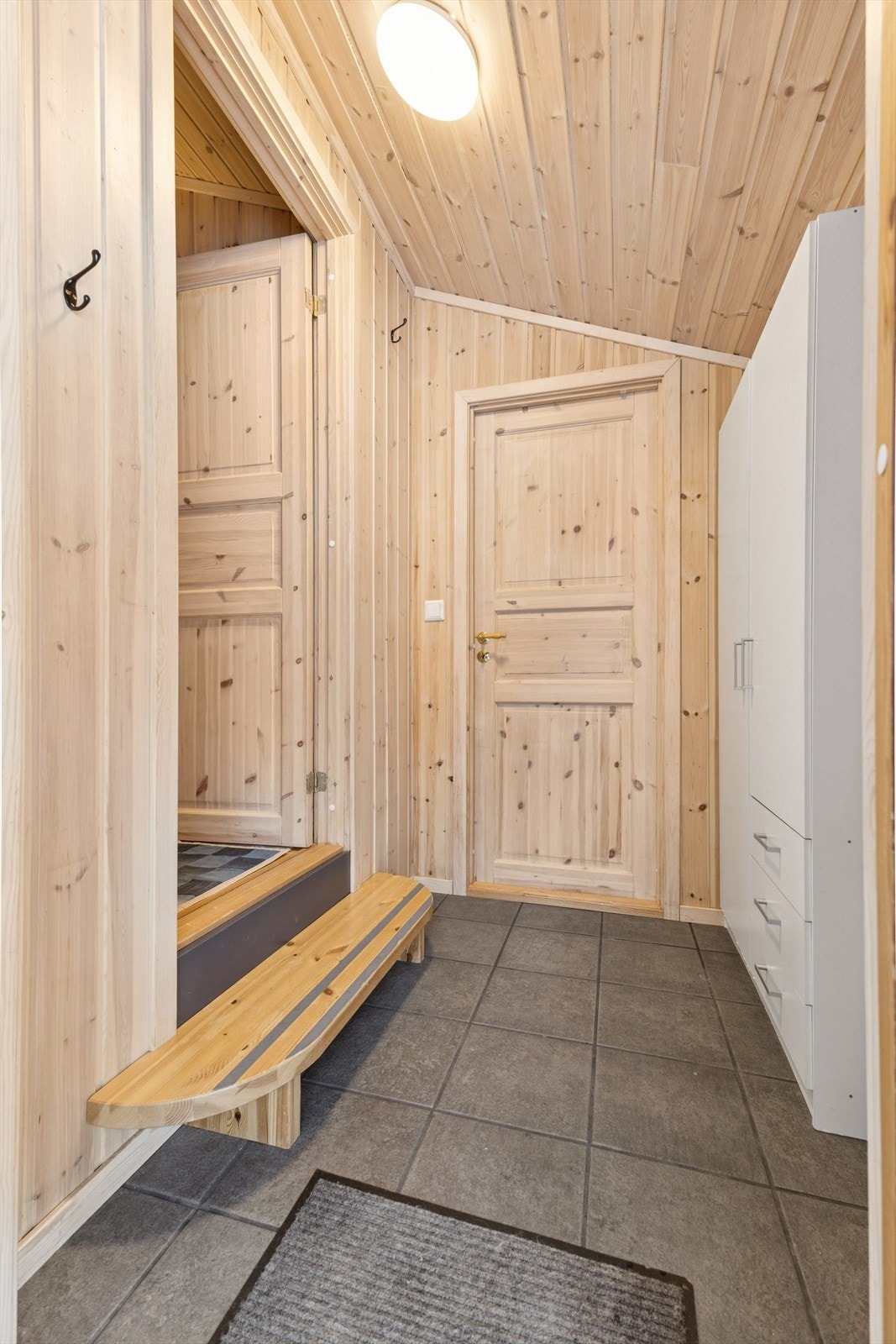 Flislagt gulv i entréen gir et praktisk og lettstelt inngangsparti. Panelte vegger og tak skaper en helhetlig og varm atmosfære. Galleribilde