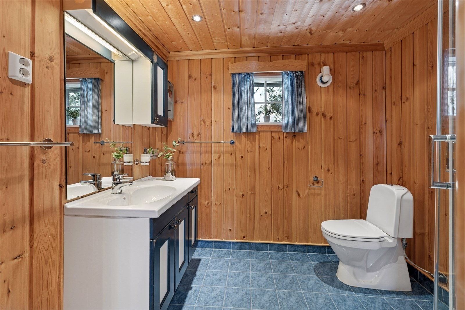 Badet er innredet med fliser på gulv med underliggende varme, heldekkende servant, servantskap, speil, dusjkabinett og gulvstående toalett. Galleribilde