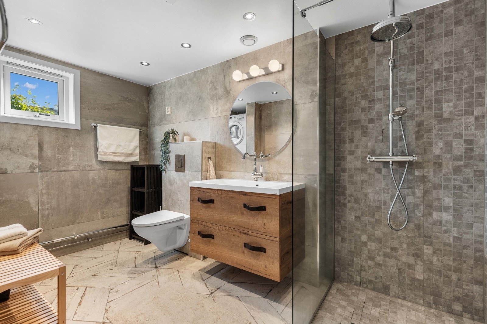 Badet er helfliset og utstyrt med vegghengt toalett, dusjhjørne med regndusj og praktisk servant med oppbevaring. Galleribilde