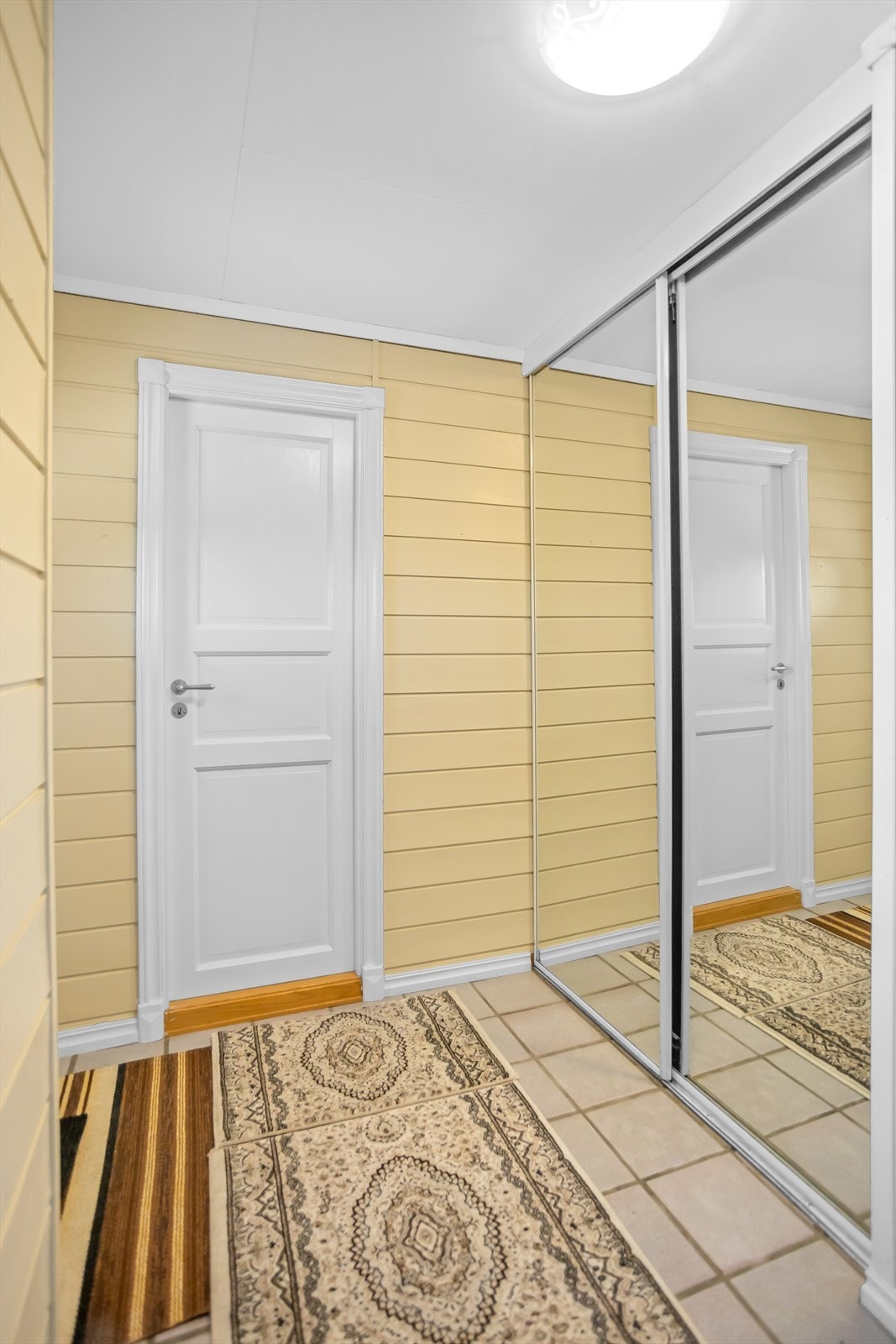 En innbydende og arealeffektiv entré med flislagt gulv og en praktisk skyvedørsgarderobe som holder rommet ryddig. Galleribilde