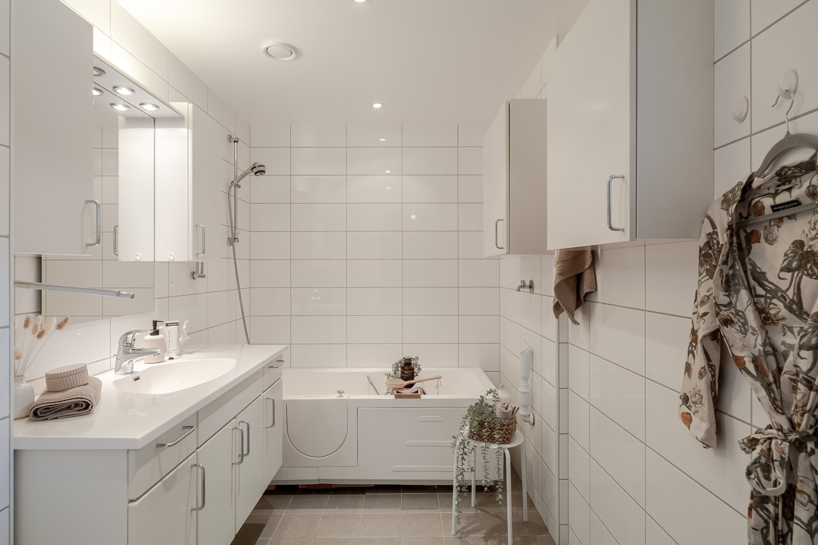 Badet er helfliset og utstyrt med vegghengt toalett, innredning med nedfelt servant, badekar og opplegg for vaskemaskin Galleribilde