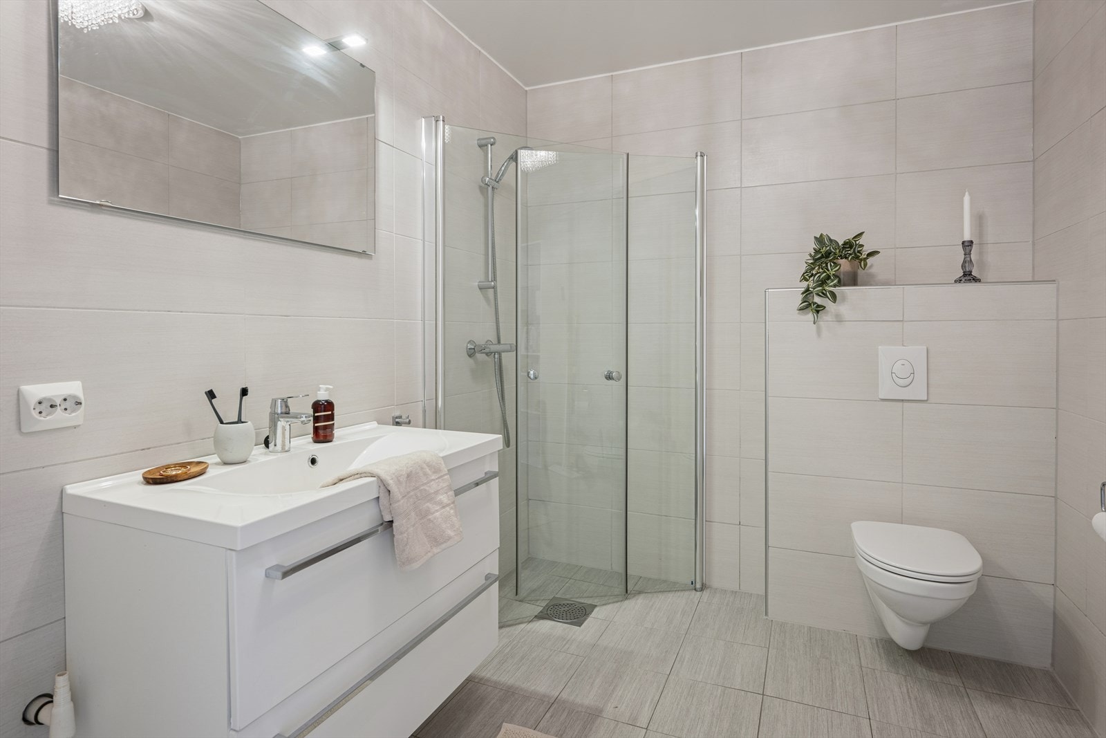 Badet i første etasje er helfliset og har vannbåren varme for ekstra komfort. Badet er ellers utstyrt med dusjhjørne, vegghengt toalett og baderomsinnredning med nedfelt servant. I tillegg har man opplegg for vaskemaskin. Galleribilde