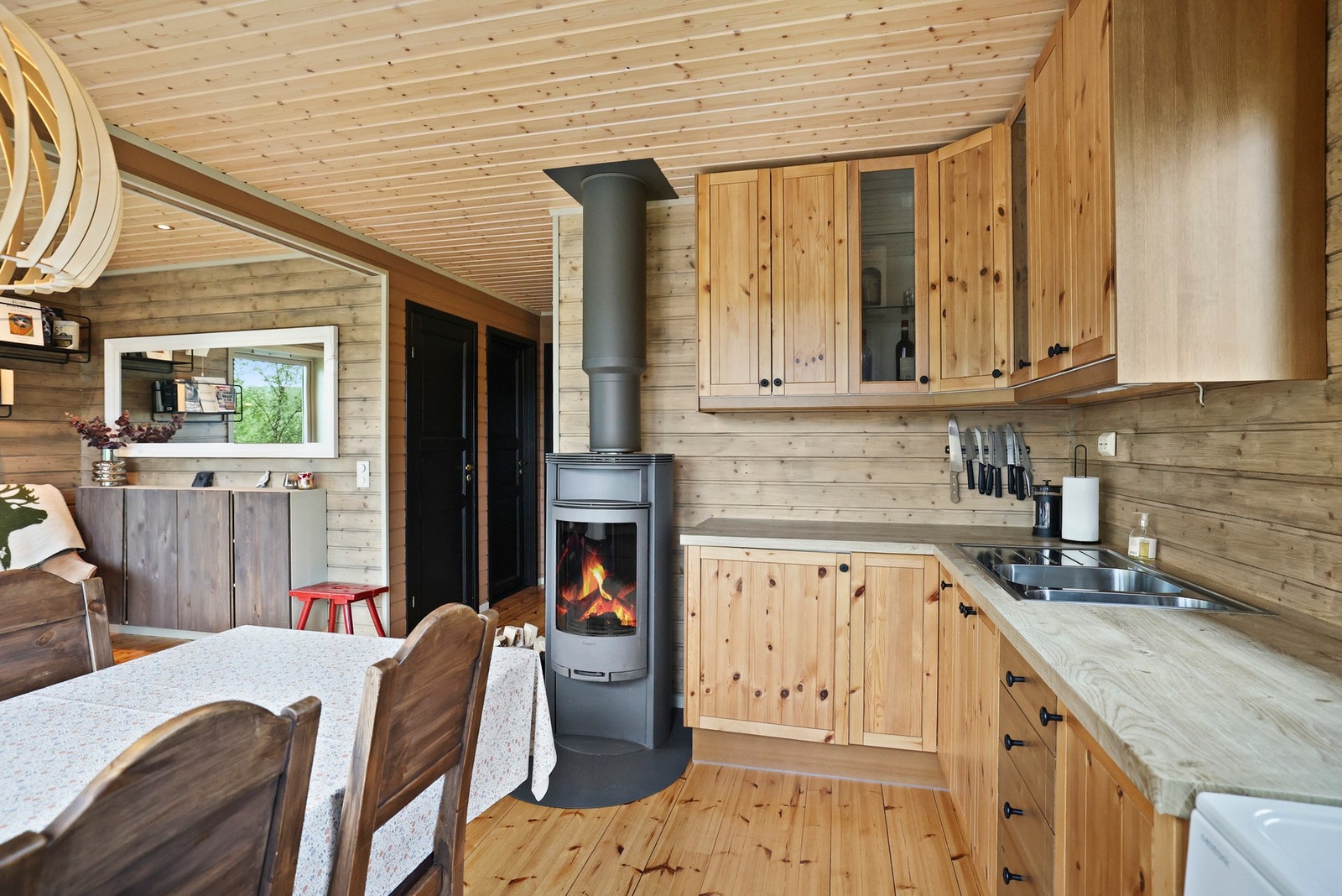 Kjøkkeninnredning med tre fronter og laminert benkeplate med nedfelt stål vaskekum, integrert ventilator og frittstående komfyr og kjøleskap. Galleribilde