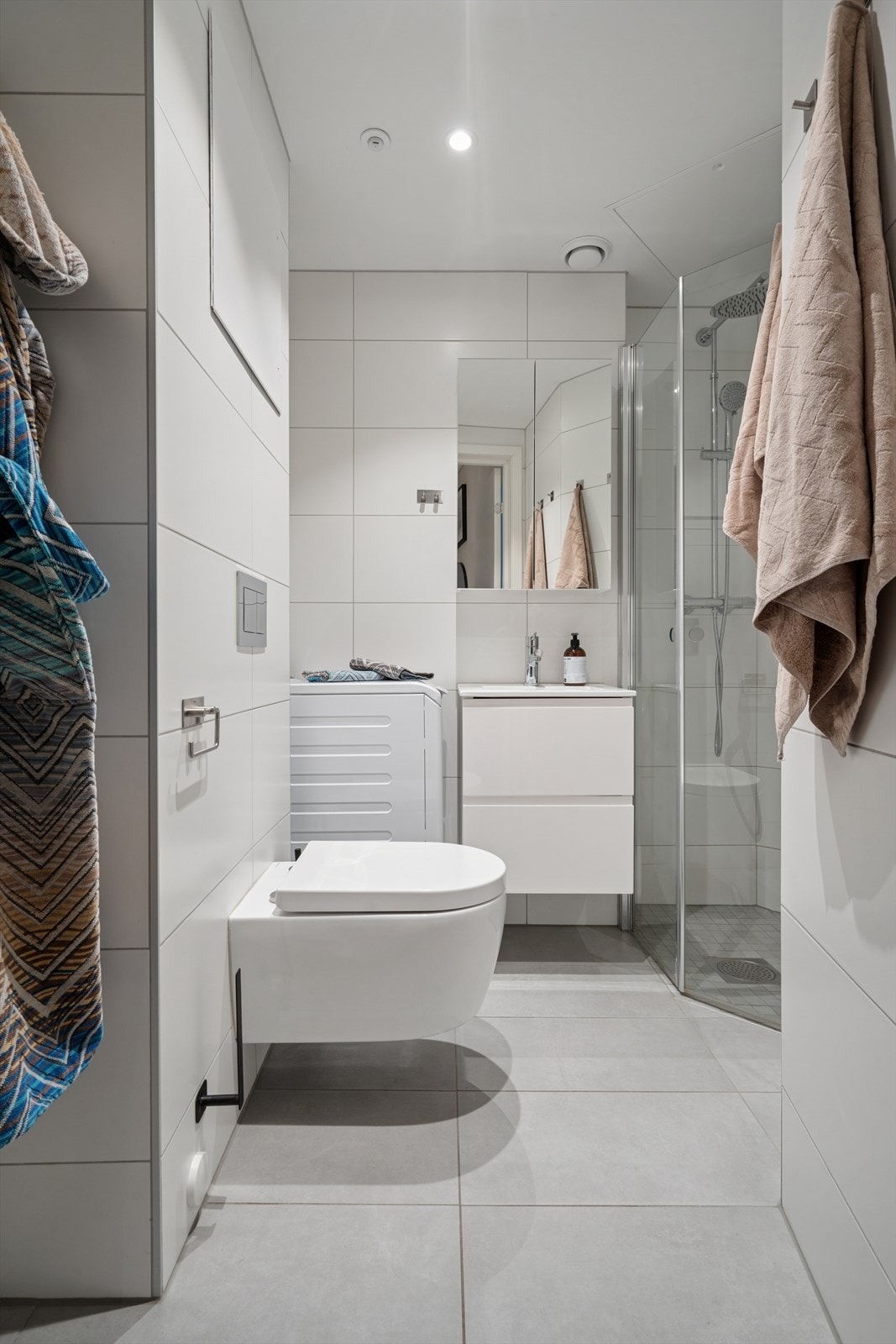 Badet er utstyrt med vegghengt toalett, dusjhjørne med glassdør, samt baderomsinnredning med nedfelt servant og opplegg for vaskemaskin Galleribilde