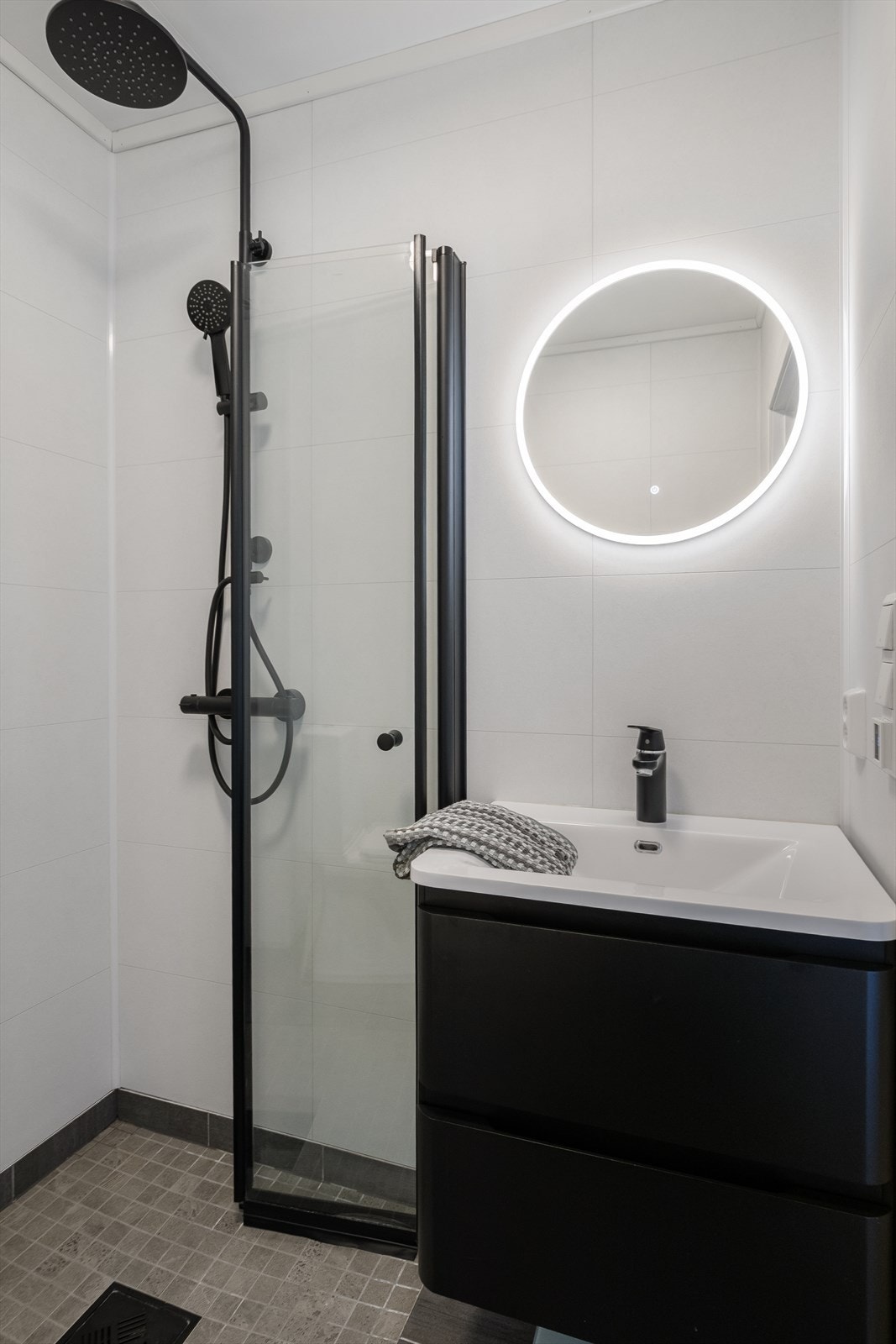 Rommet er innredet med et moderne servantskap med servant, et gulvmontert toalett og en vegghengt dusj med skjermdører i herdet glass. Galleribilde