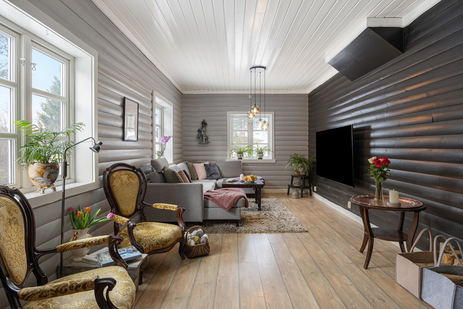 Allrommet har store sprossevinduer, gråmalt, liggende panel på veggene og tidsmessig laminat på gulvet. Galleribilde