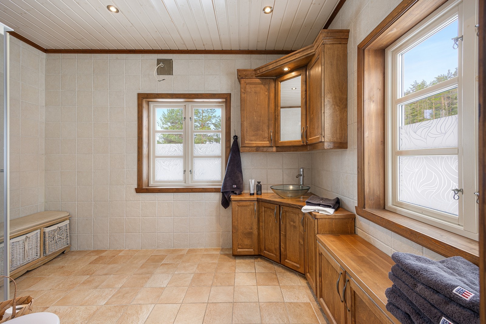 Baderomsinnredningen har gylne, profilerte fronter og består av en toppmontert servant på en skapseksjon, veggskap, speilskap og sittebenk med oppbevaring. Galleribilde