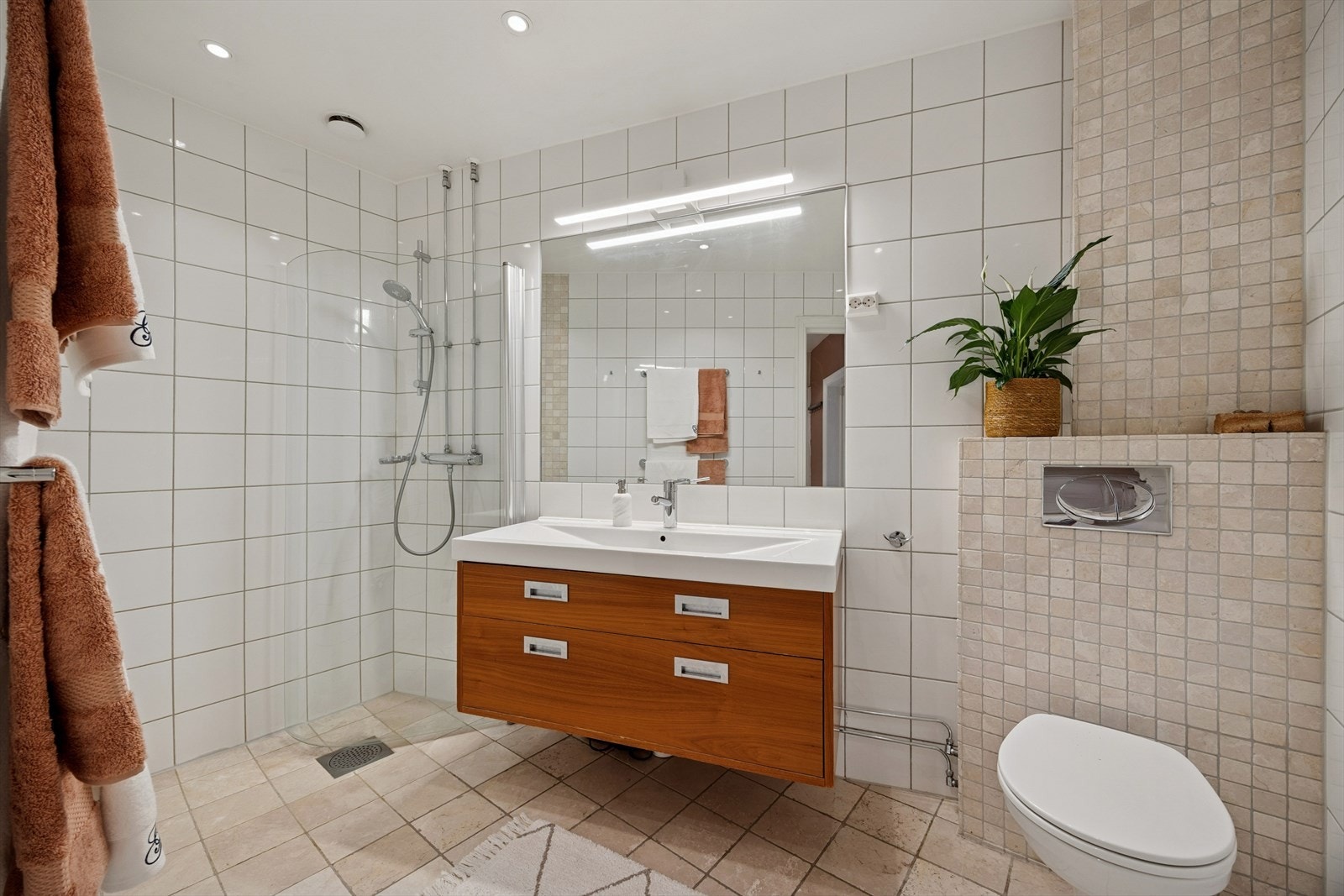 Koselig baderom med servant og benkeskap, stort speil med overbelysning og varmekabler i gulvet. Galleribilde