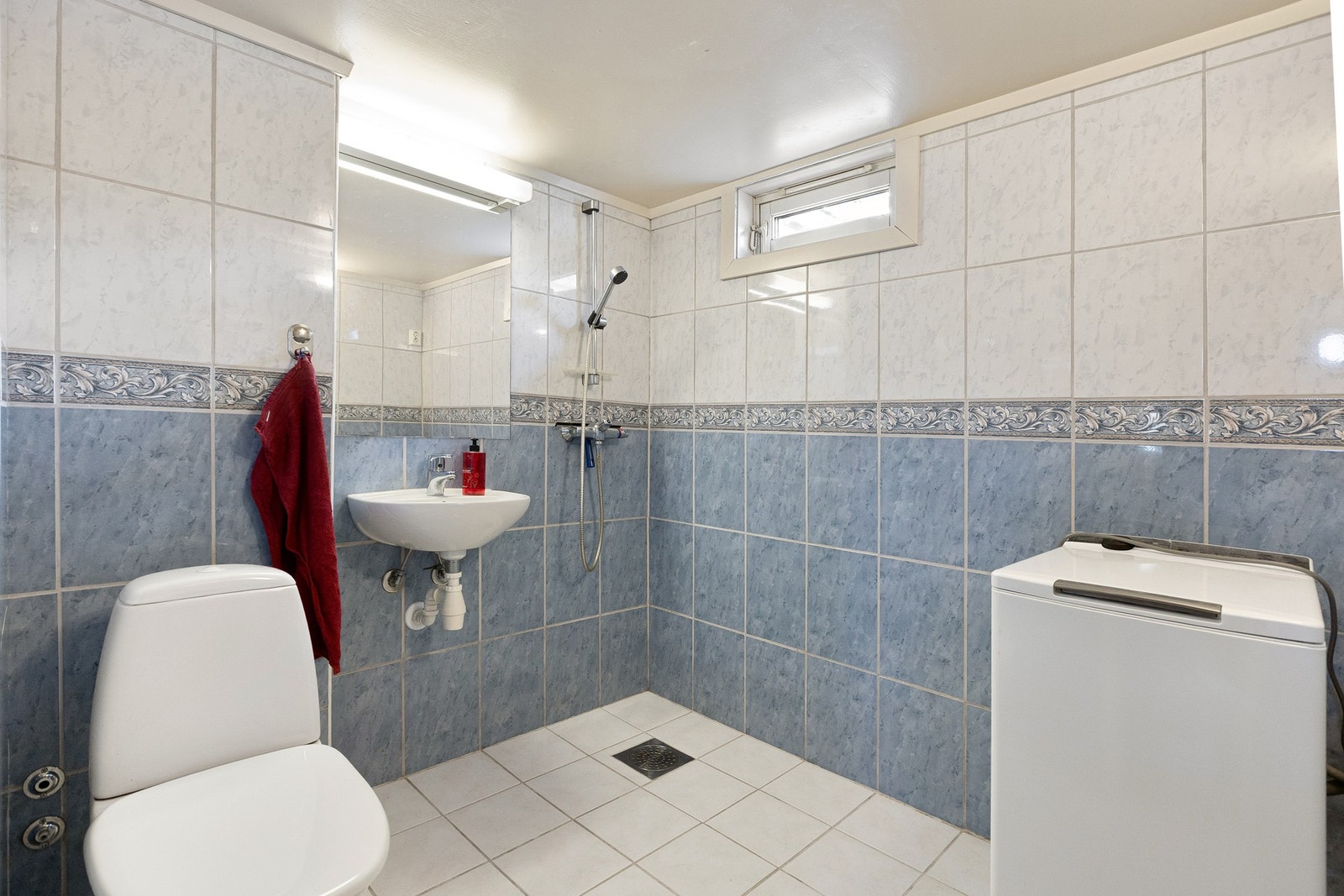 Badet har flislagte overflater, elektrisk gulvvarme, dusj på gulv, servant, gulvstående toalett og opplegg for vaskemaskin. Galleribilde