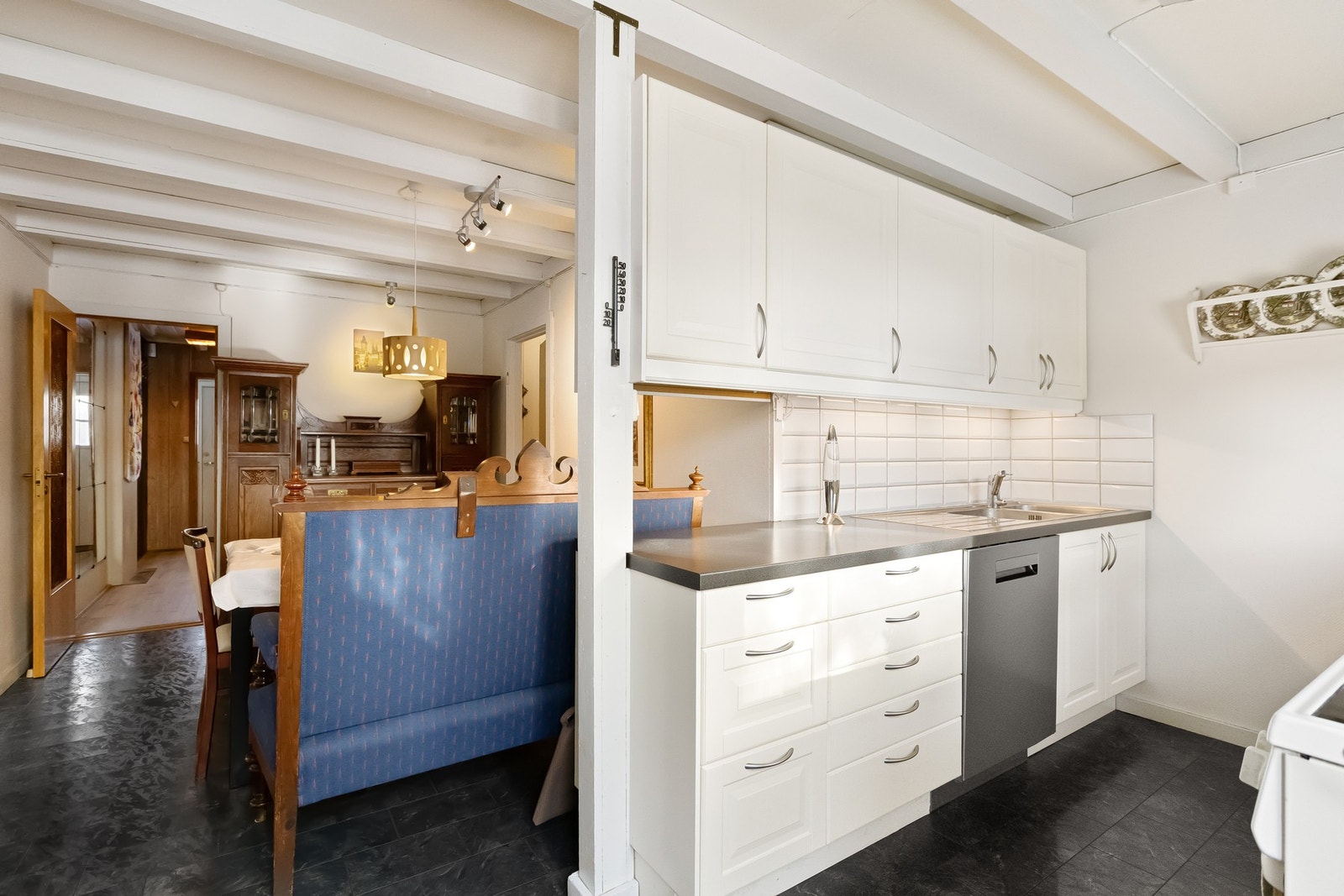 Det er fliser på vegg over benkeskap og opplegg for oppvaskmaskin. Galleribilde