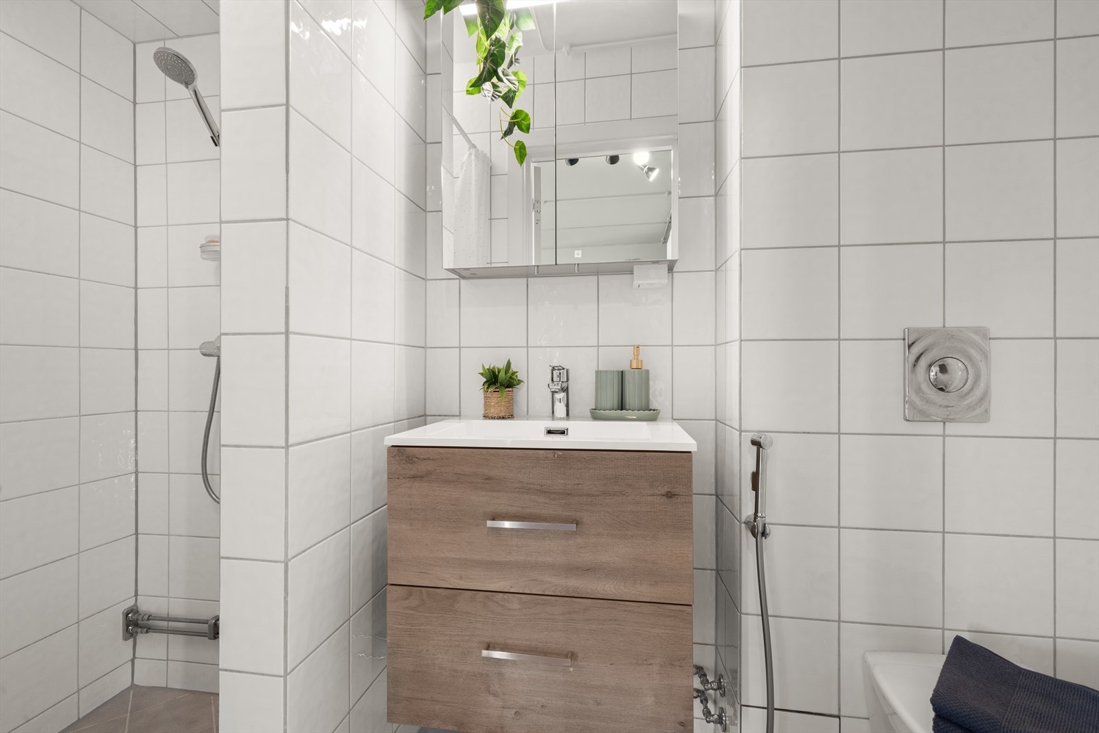 Baderomsinnredningen består av dusj direkte på gulv med termostat batteri, veggmontert klosett, håndholdt bide, servant med skuffer og speilskap med belysning. Galleribilde