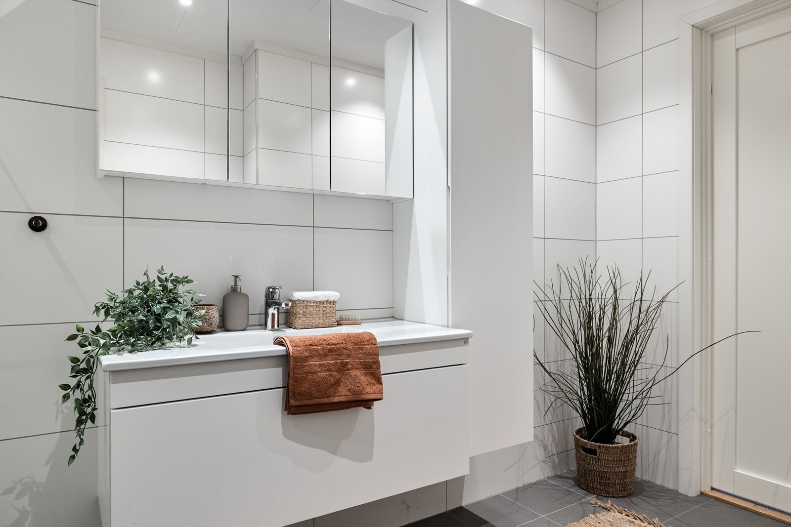 Flott baderomsinnredning med hvite glatte fronter og heldekkende servant, speilskap med belysning over og ekstra vegghengt høyskap ved siden av. Galleribilde