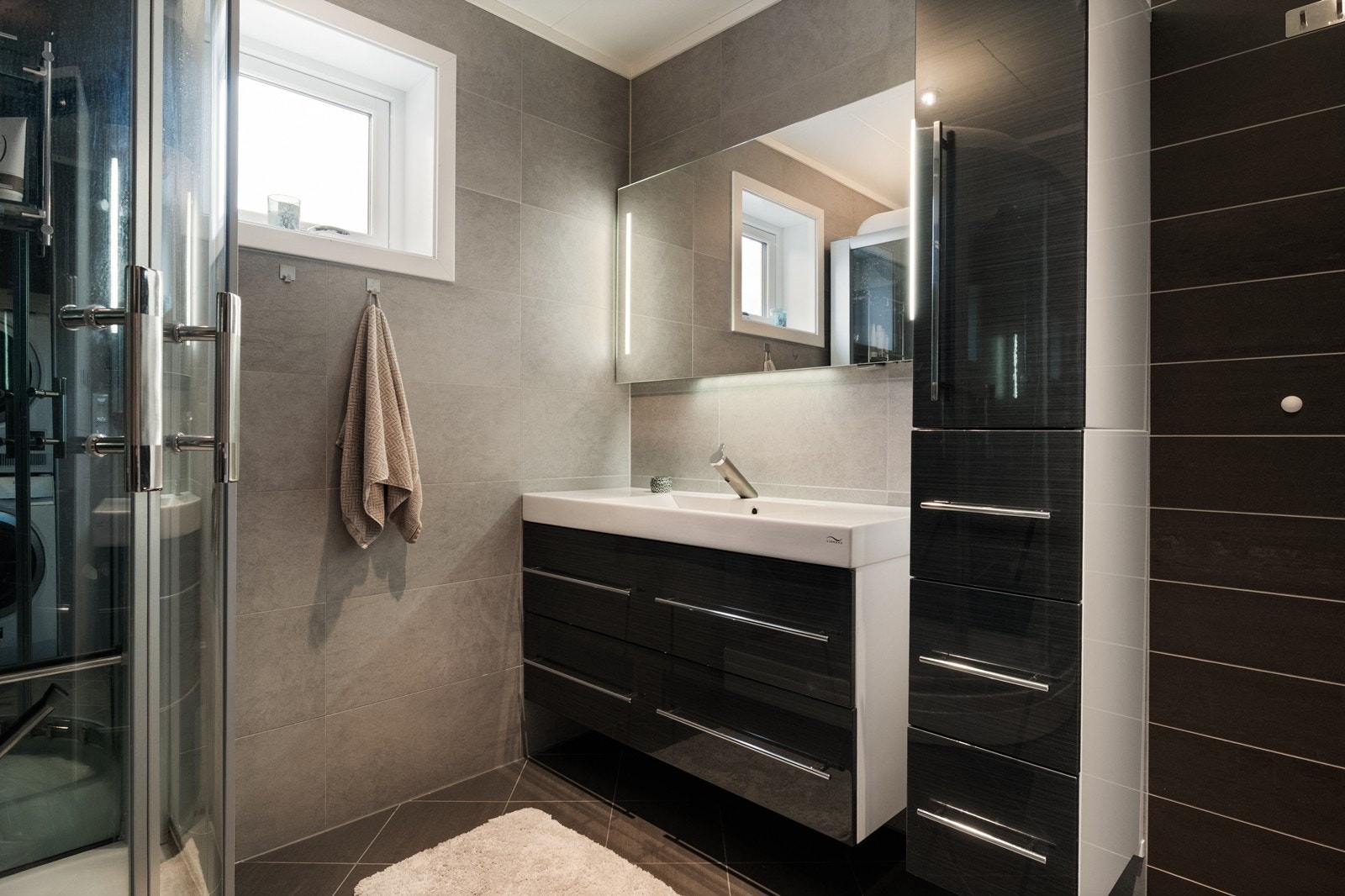 Badet er utstyrt med mørk baderomsinnredning med heldekkende servant, under- og høyskap og speil med integrert lys. Galleribilde