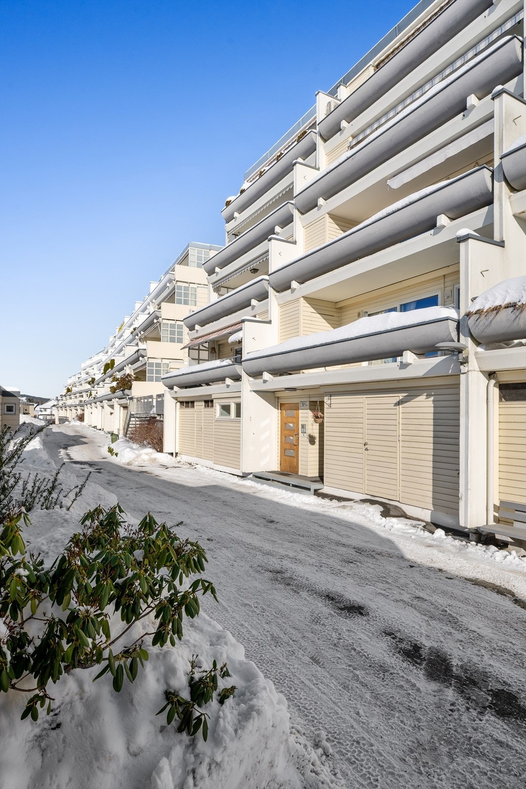 Hit og dit: Inngangspartiet er ryddig og oversiktlig, med en tydelig oppgangsdør utstyrt med porttelefon som sikrer enkel adgang til leiligheten. med adkomst til garasje og avfallsrom henholdsvis cirka to og fire steg til høyre for døren på bildet. Galleribilde