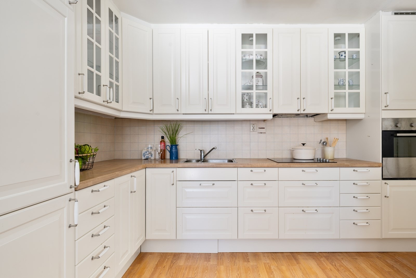 Gastronomisk spillerom: Innredningen er fra IKEA (ca. 2012) og har hvite, profilerte fronter som gir et tidløst og klassisk uttrykk. Vitrineskapene tilfører et elegant preg og gir mulighet for å vise frem servise og glass på en dekorativ måte. Galleribilde