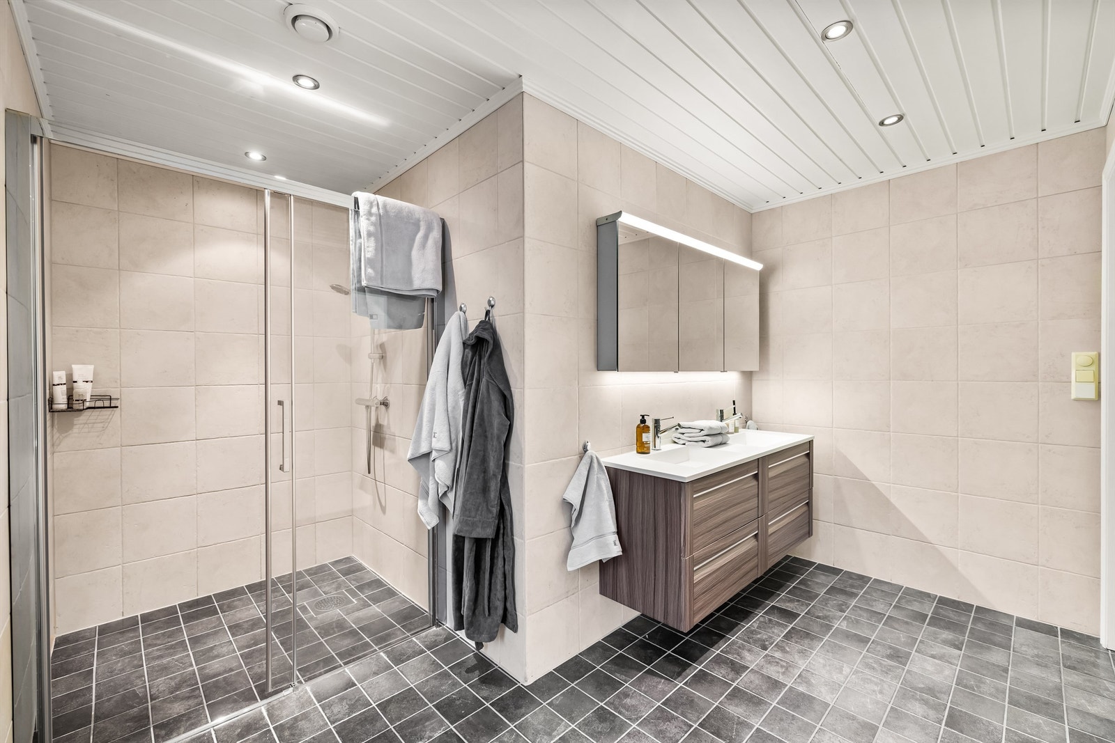 Bad en suite med flislagt gulv med varme, dusjnisje med glassdør og downlights i taket. Dobbelservant forenkler hverdagslogistikken på badet. Galleribilde