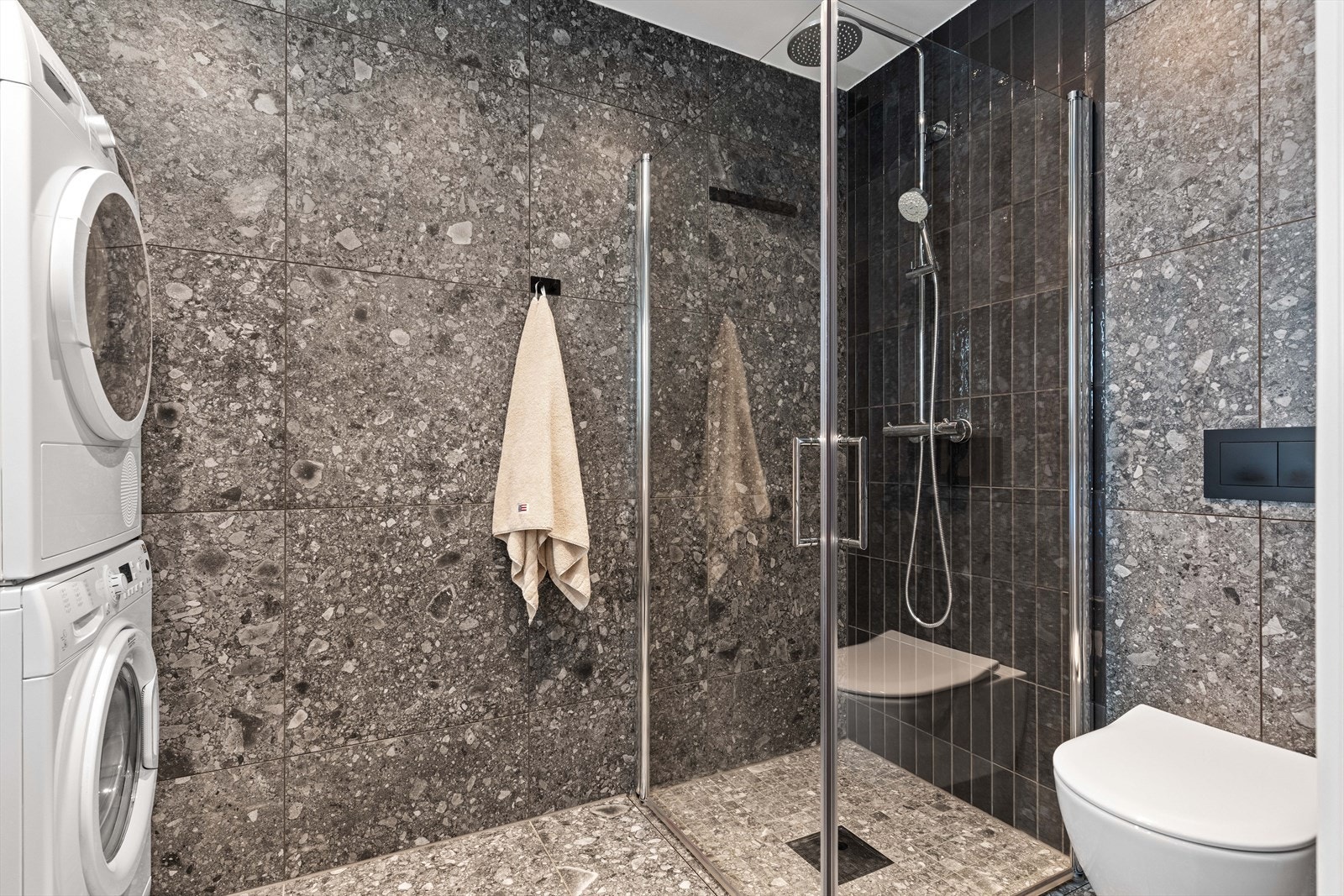 Badet er videre utstyrt med heldekkende servant med servantskuffer, regnfallsdusj m/innfellbare glassdører, vegghengt toalett og opplegg for vaskemaskin og tørketrommel. Galleribilde