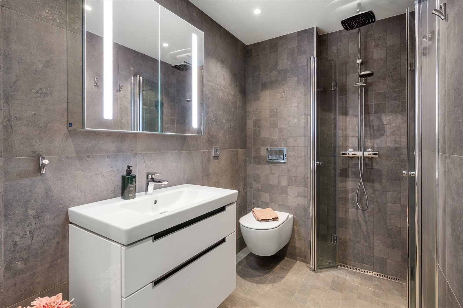 Bad 2: flislagt baderom med innfelt belysning i himlingen, vegghengt toalett, dusj direkte på gulv med innfellbare dusjdører og en praktisk servantinnredning. Galleribilde