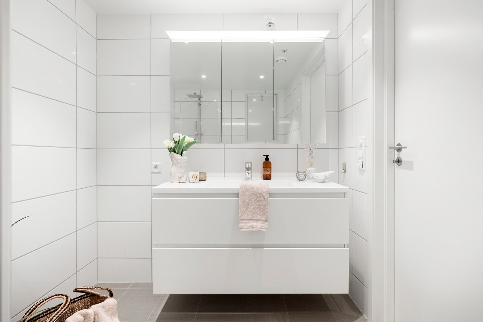 Rommet er innredet med vegghengt toalett, heldekkende servant på skuffeseksjon, speil med belysning og dusjhjørne med regnfallsdusj og innfellbare glassvegger Galleribilde