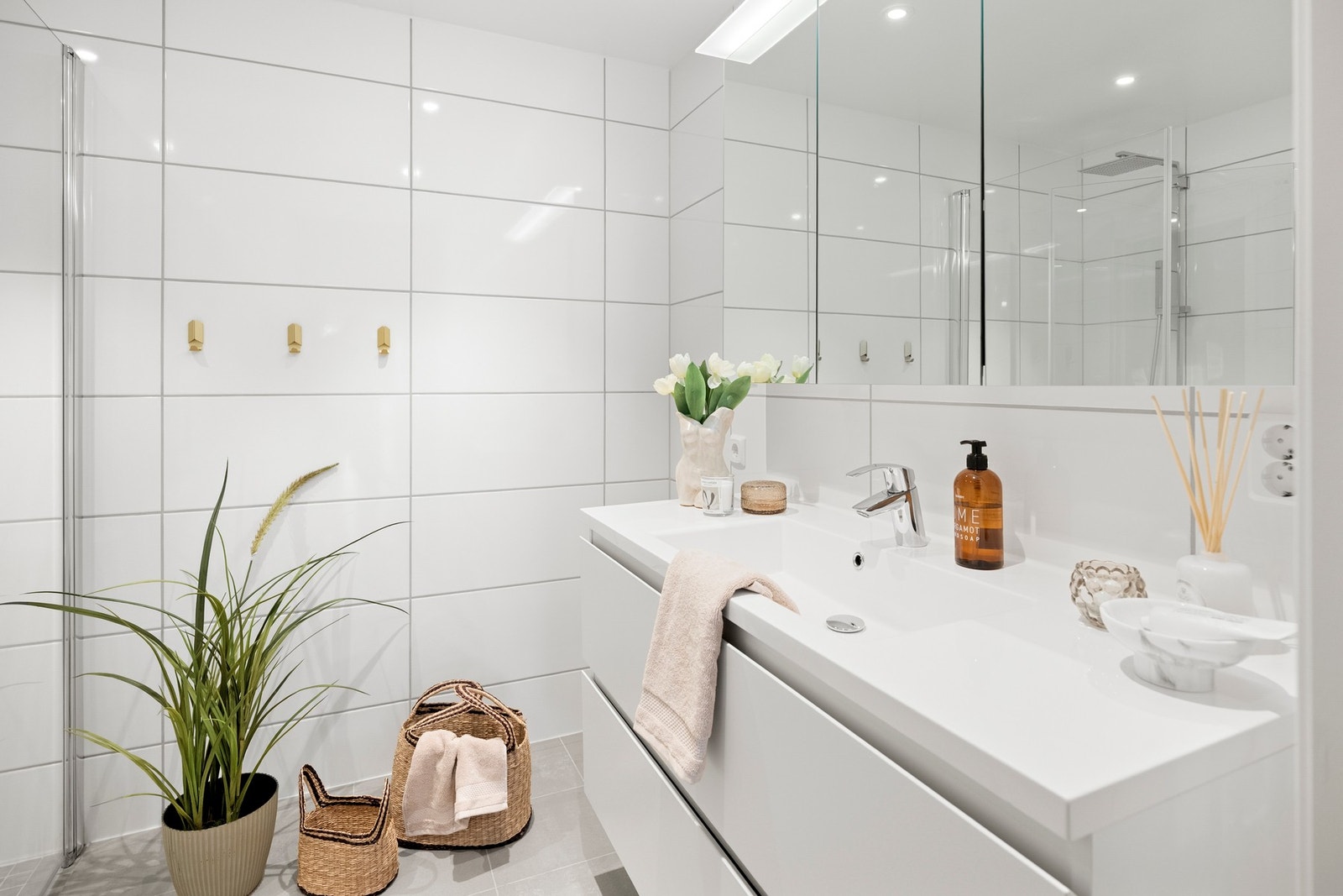 Rommet er innredet med vegghengt toalett, heldekkende servant på skuffeseksjon, speil med belysning og dusjhjørne med regnfallsdusj og innfellbare glassvegger Galleribilde