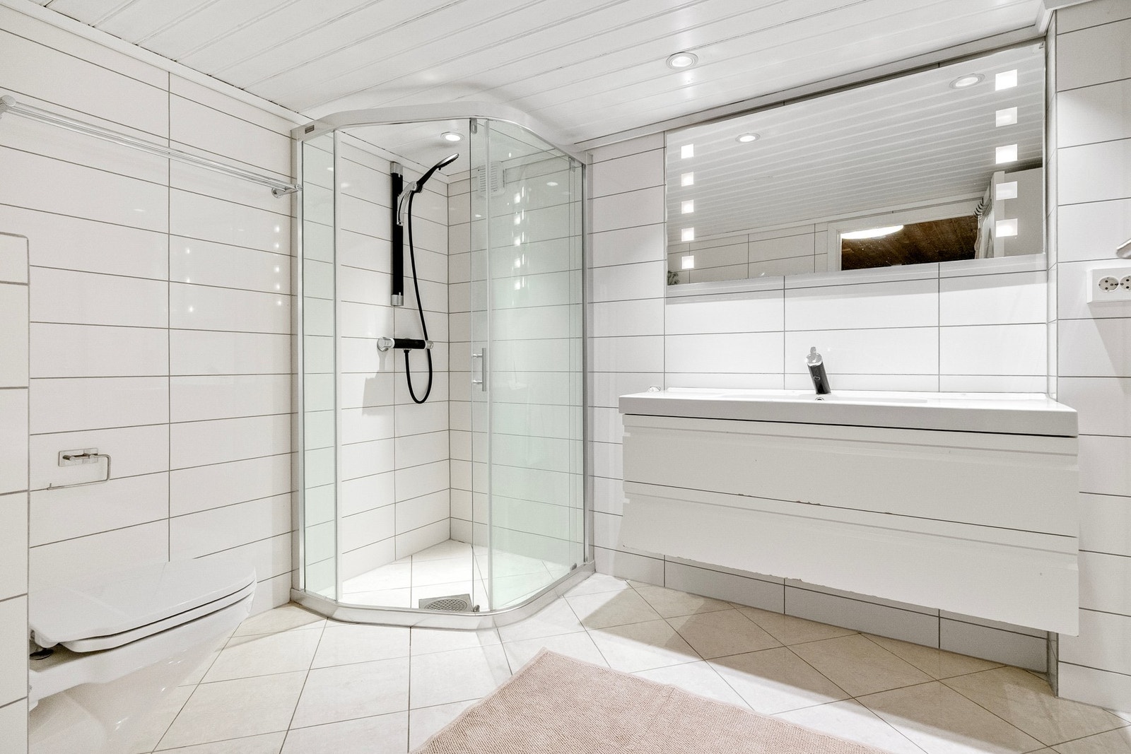 Her er vegghengt toalett, servant med tilhørende innredning og høyskap, samt dusjsone med glassvegger. Galleribilde