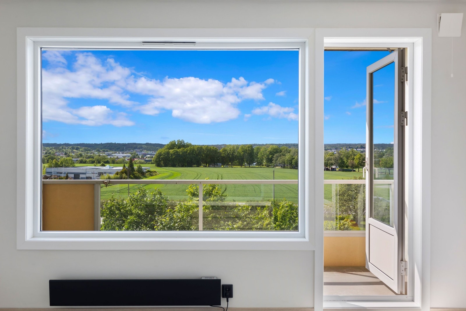 Vestvendt, solrik og grønn utsikt fra stort vindu mot veranda. Galleribilde