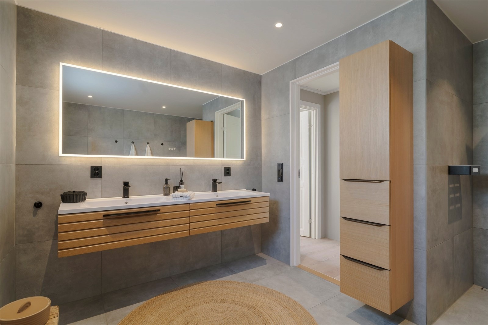 Badet har stor, flislagt dusjsone med regndusj, vegghengt toalett og dobbel servant i heldekkende innredning med god oppbevaringsplass. Galleribilde