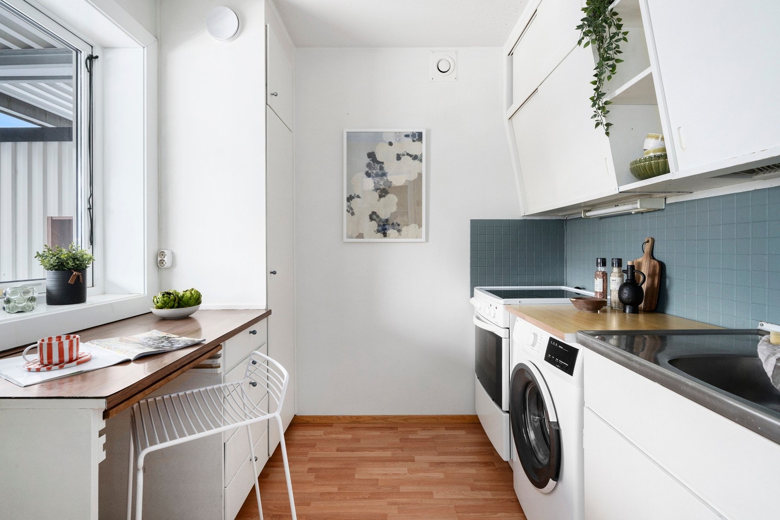 Leilighetens kjøkken har slette flater, benkeplater av laminat og fliser mellom benk og overskap Galleribilde