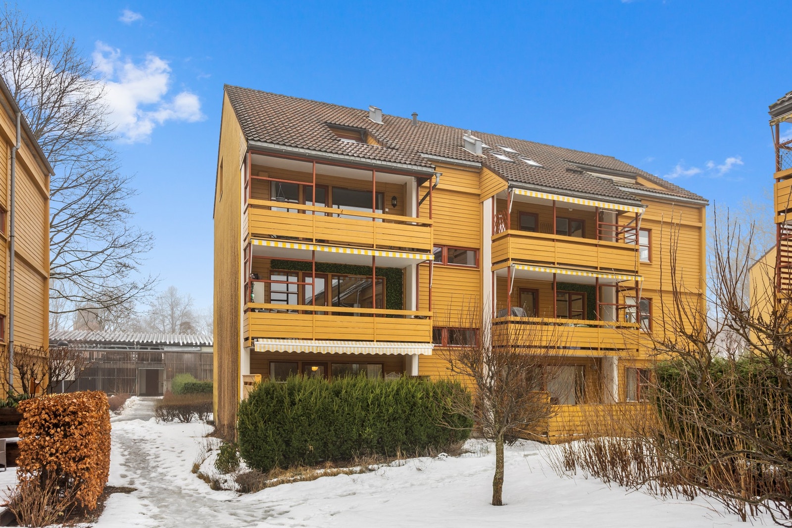 Fasade fra grøntområde. Leiligheten ligger i 1. etasje på venstre side. Terrassen er skjermet med en hekk. Galleribilde