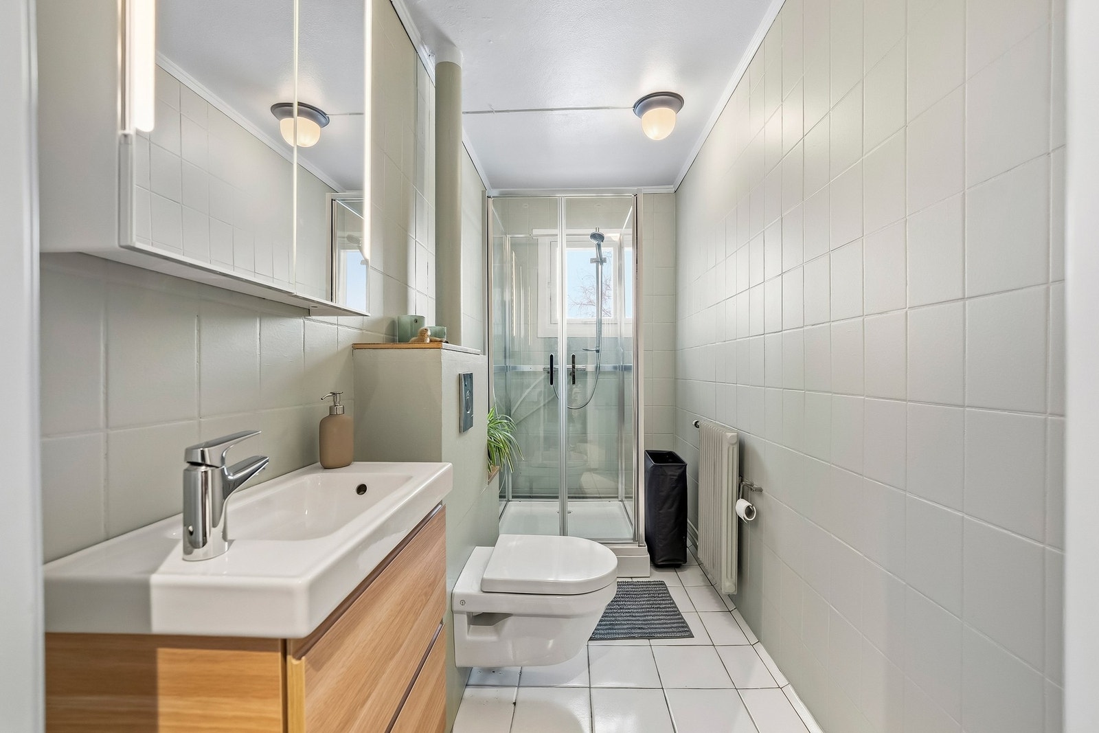 Lyst, helfliset baderom, baderomsinnredning med skuffer og helstøpt servant, speilskap med lys, dusjkabinet og vegghengt toalett Galleribilde