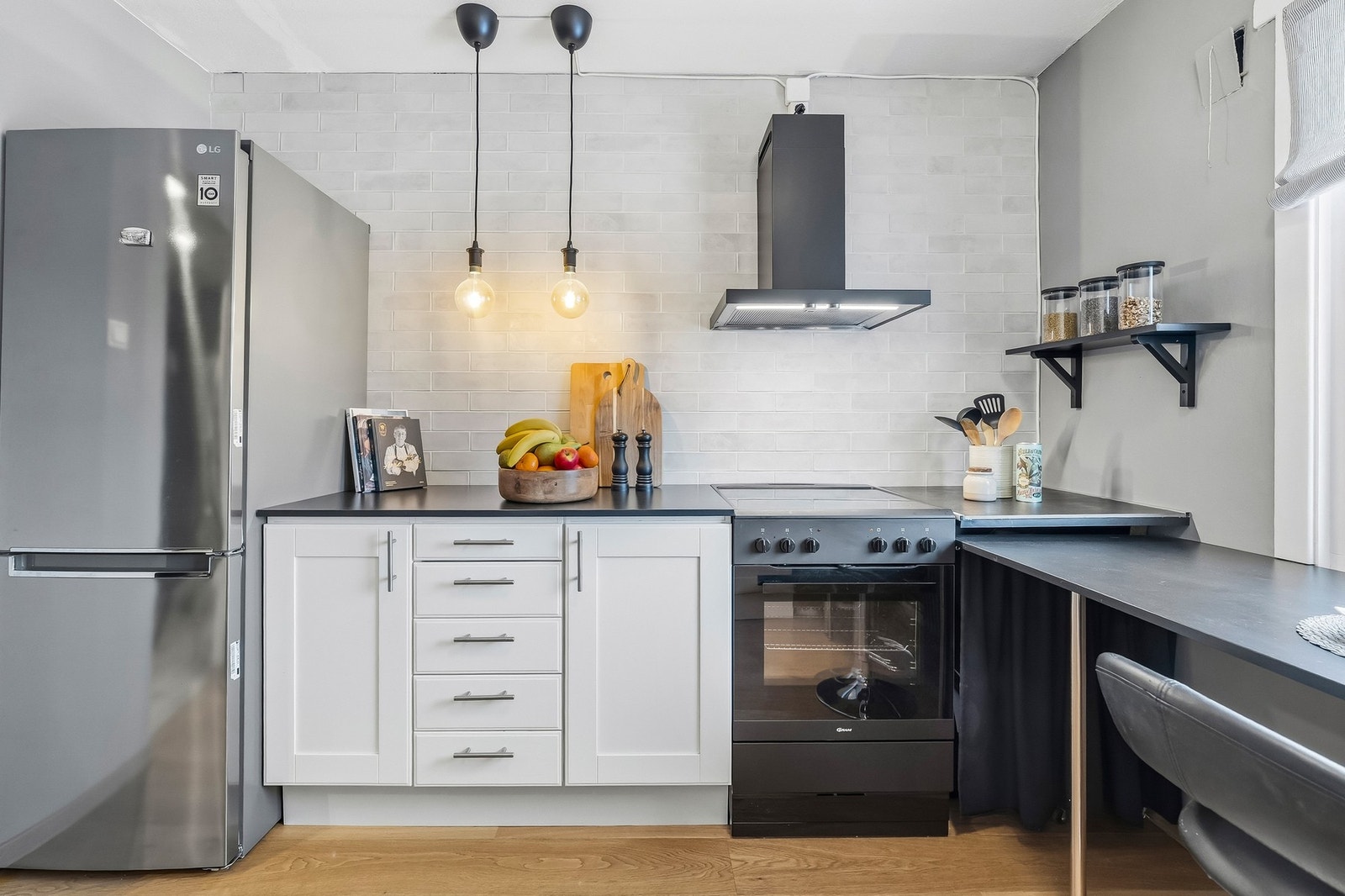 Lyst og trivelig kjøkken med lys, profilert kjøkkeninnredning og mørk benkeplate Galleribilde