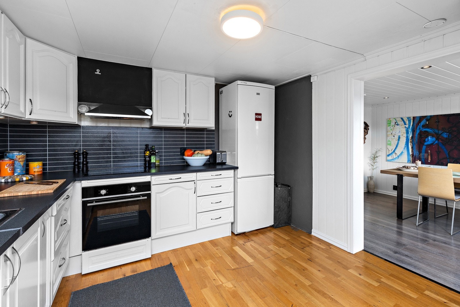 Lys og funksjonell kjøkkenløsning med fliser og vinyl mellom benk og overskap. Galleribilde