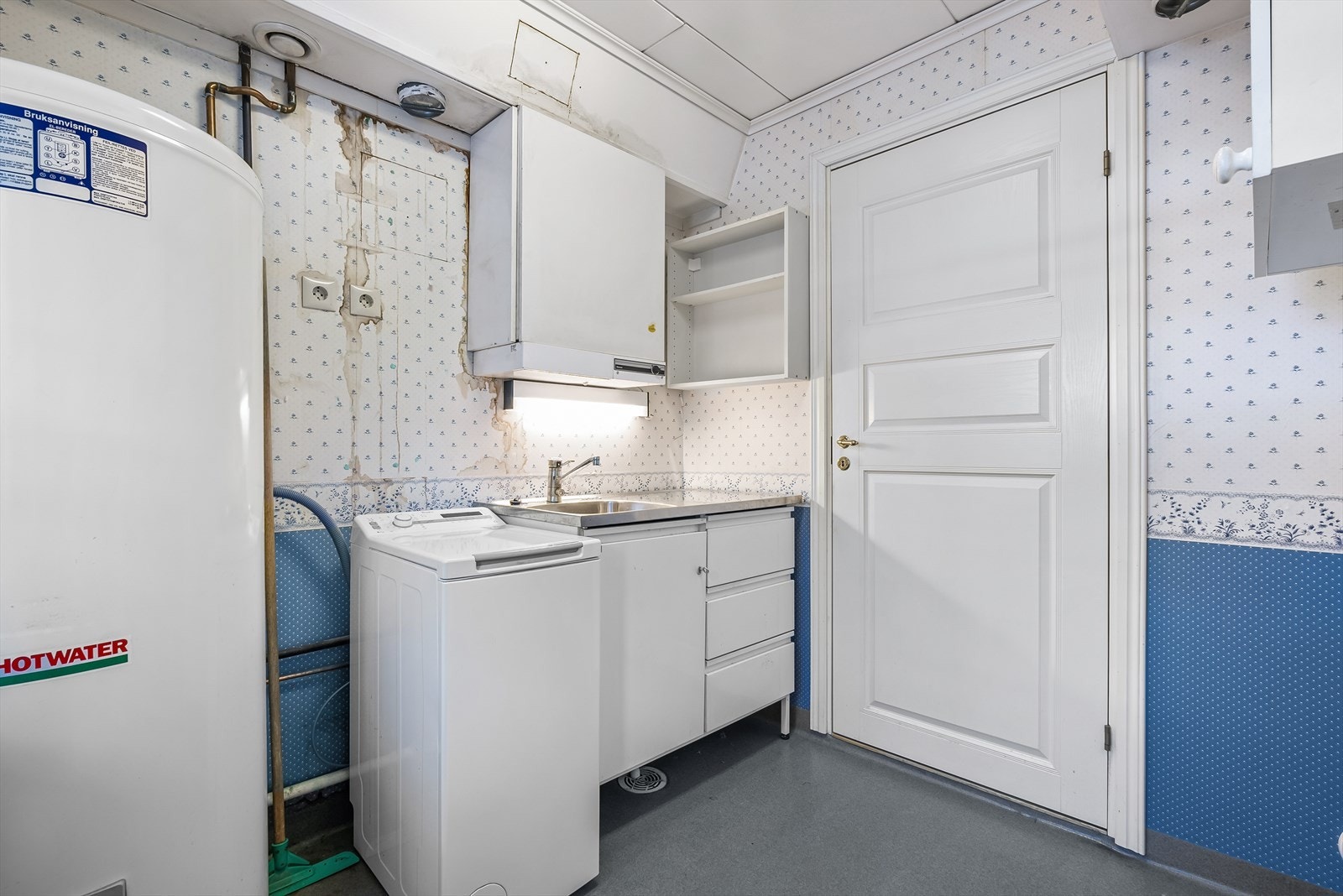Praktisk vaskerom fra byggeår. Rommet er innredet med en vaskekum, varmtvannsbereder og opplegg til vaskemaskin og tørkemaskin Galleribilde
