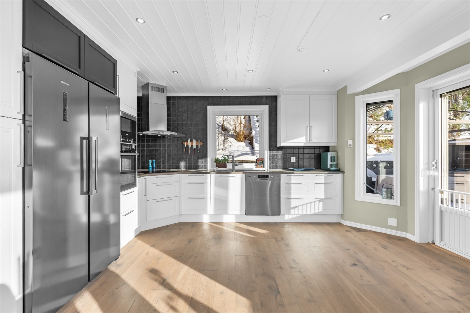 Fritthengende ventilator og integrerte hvitevarer. Det er lagt sorte fliser over benkeskapene. Galleribilde