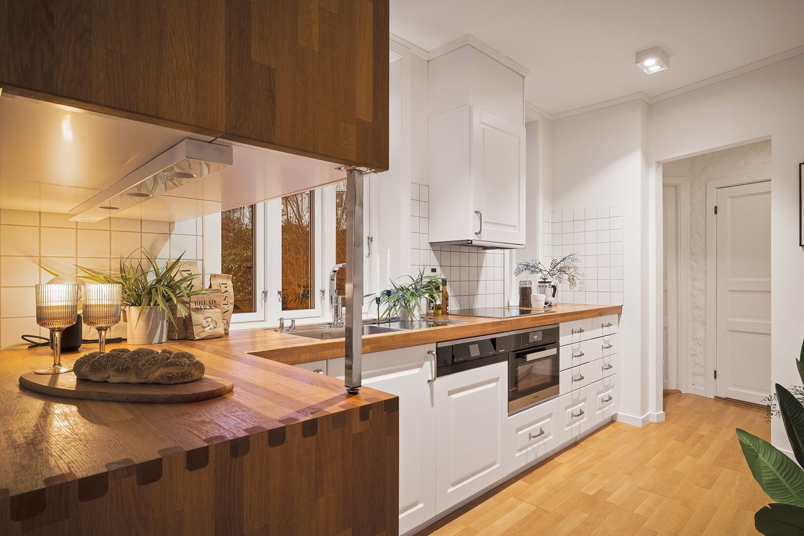 Kjøkkenet har et moderne uttrykk og er innredet med hvite profilerte fronter med demper, skrog av finèr. Benkeplater i heltre, samt nedfelt stål vaskebeslag og platetopp. Galleribilde