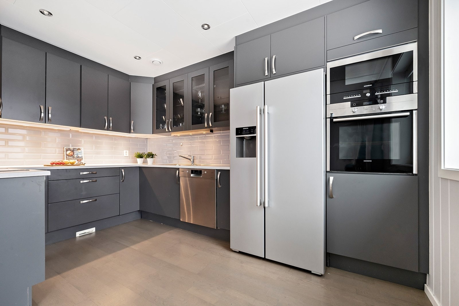 Kjøkkenet har innredning med glatte fronter i mørk grå farge, benkeplate av laminat med nedfelt vask og benkebeslag i stål. Galleribilde