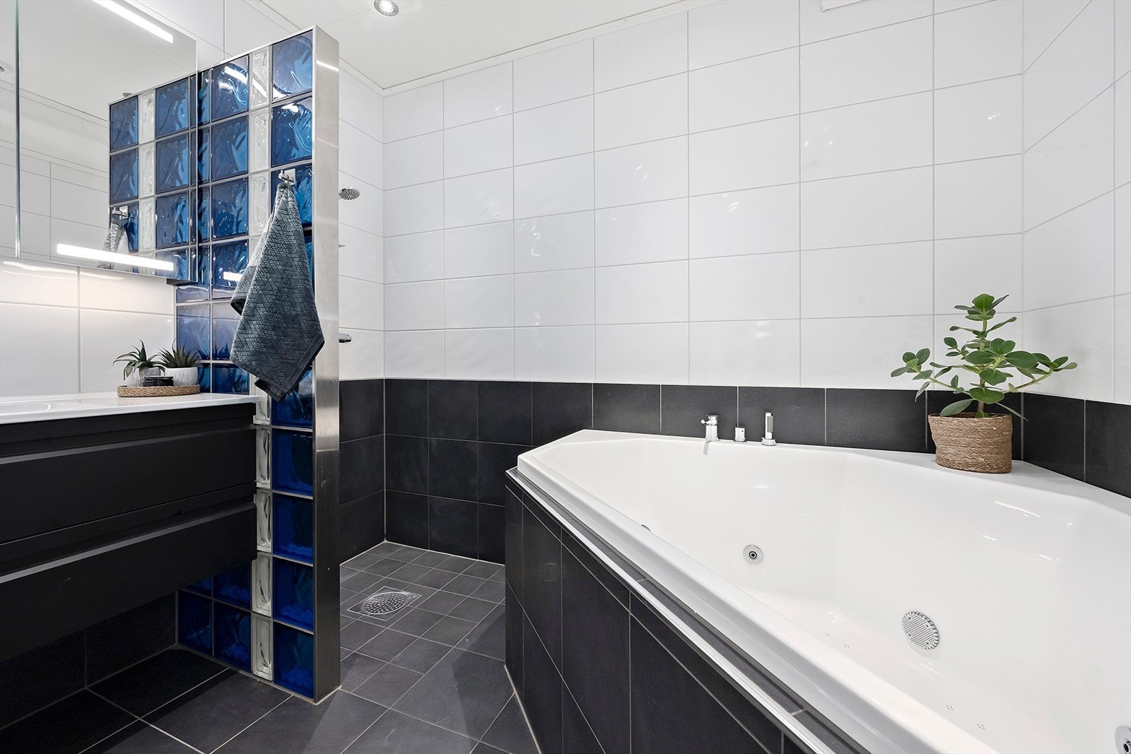 Badet er innredet med innebygget hjørneboblebadekar, heldekkende servant, speilskap med belysning, dusjnisje og vegghengt toalett. Galleribilde