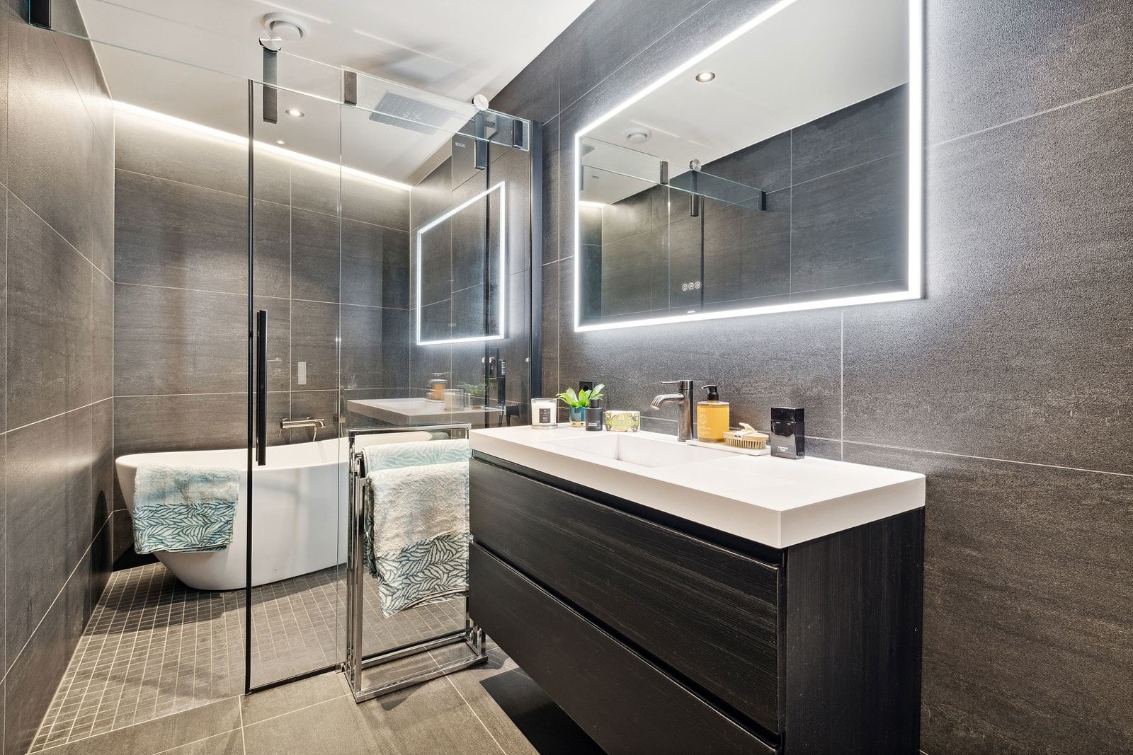 badet ligger mellom to soverom og er innredet med veggmontert dusjtoalett fra Grohe Sensia med fjernkontroll, Corian servantinnredning og dusjnisje med glassdør, regndusj og badekar Galleribilde