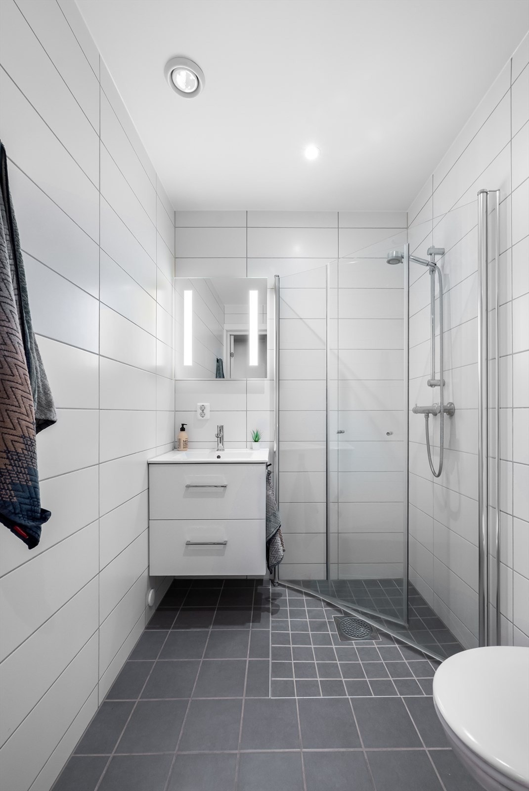 Badet er utstyrt med veggmontert toalett og dusjhjørne med innfellbare vegger. Galleribilde