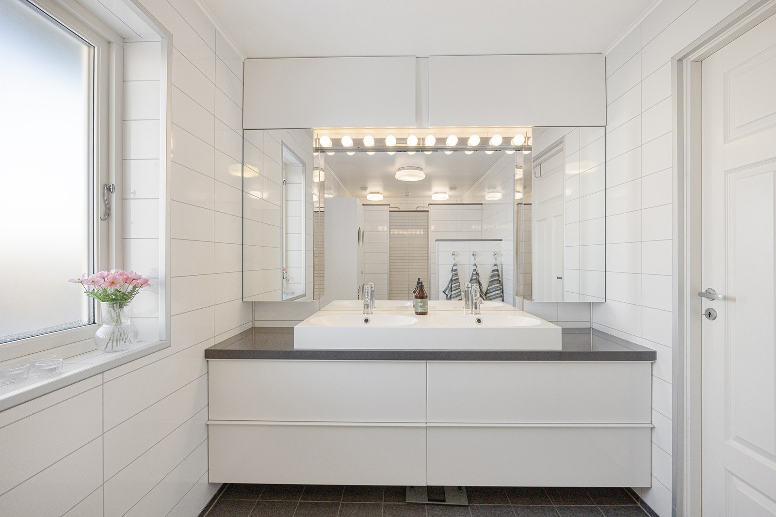 Innredningen har hvite skuffefronter med toppmontert dobbelservant og stort speil med belysning. Galleribilde