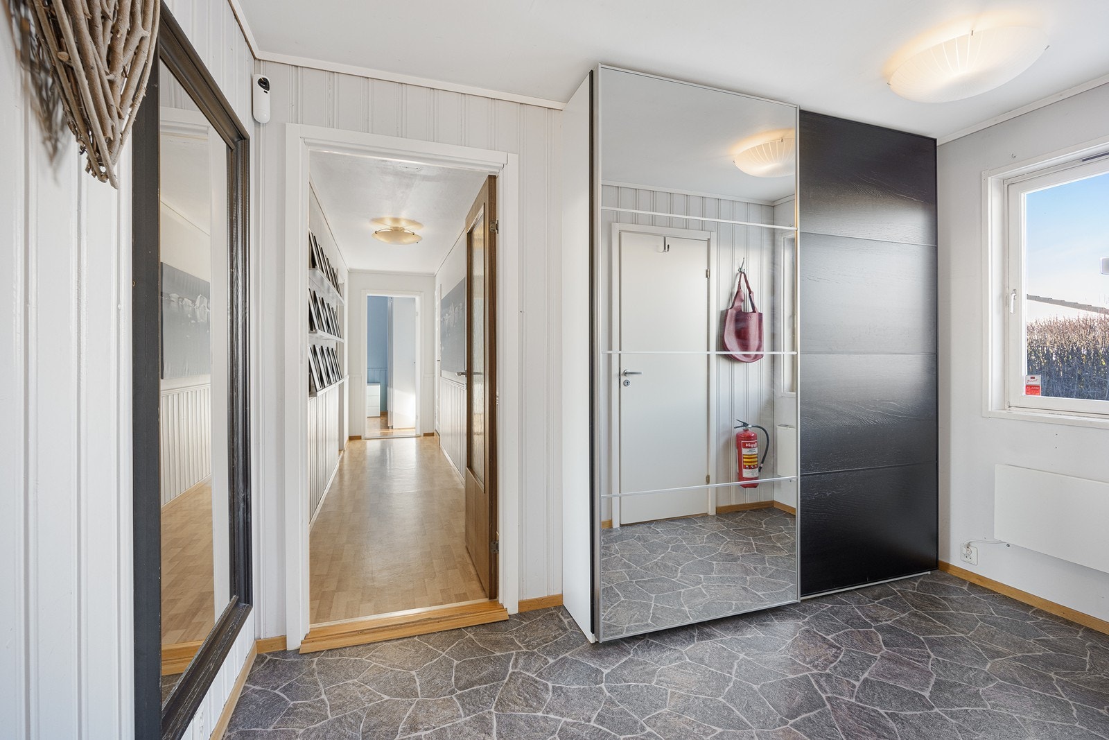 Videre inn ligger en gang med praktisk skyvedørsgarderobe for oppbevaring av ytterklær og sko. Både entré og gang har pent gulvbelegg i skiferimitasjon. Galleribilde