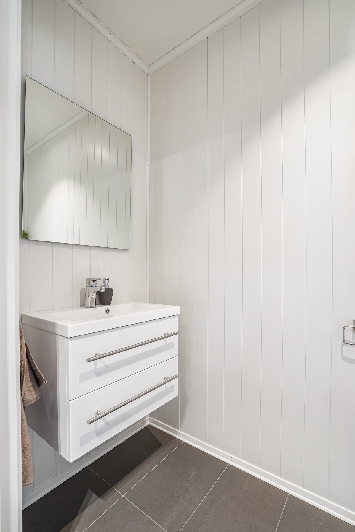 Separat toalettrom med flislagt gulv og malt panel på veggene. Innredning med skuffefronter og helstøpt servant over. Utstyrt med vegghengt toalett. Galleribilde