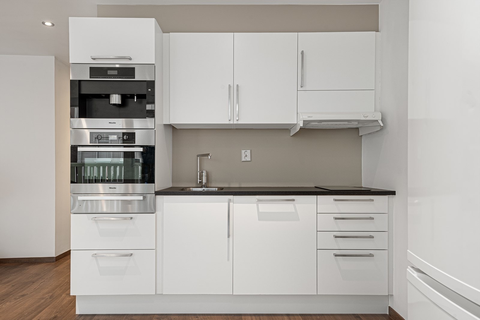Kjøkkenet er praktisk og funksjonell, med kjøl/fryseskap, oppvaskmaskin, platetopp, stekeovn og integrert kaffemaskin. Benkeplaten er i slitesterk laminat, og innredningen har moderne, glatte fronter som gir et stilrent uttrykk. Galleribilde