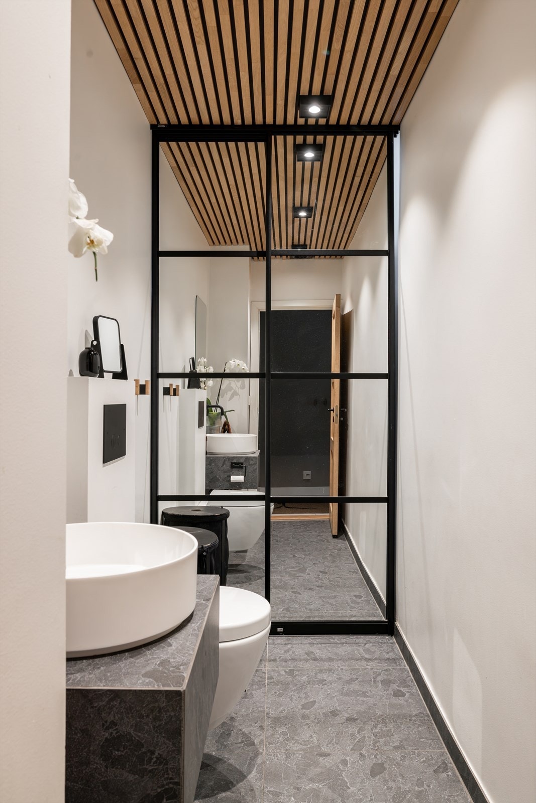 Elegant og moderne toalettrom med flislagt gulv med gulvvarme, spilehimling med downlights og stilrene detaljer Galleribilde