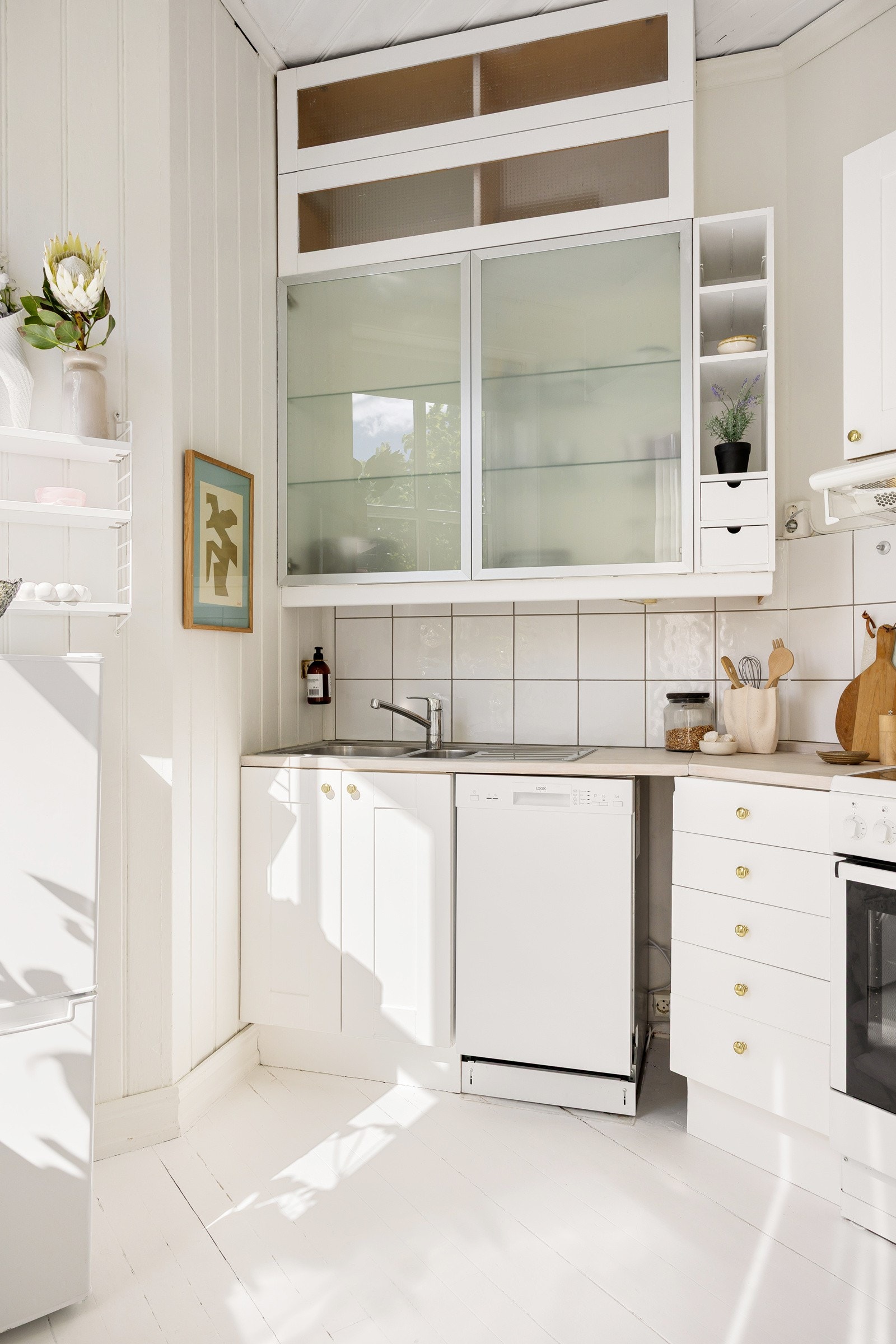 Kjøkkeninnredning med profilerte glatte fronter, overskap med fronter i frostet glass, benkeplate i heltre med nedfelt kum i rustfritt stål, fliser på vegg over benk. Galleribilde