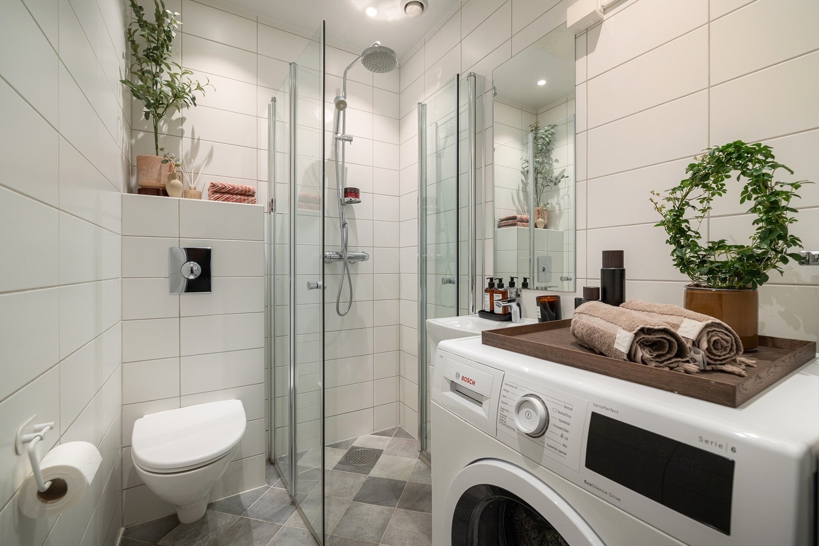 Leilighetens bad er helfliset og innredet med servant med underskap, vegghengt speil, dusjhjørne, WC og opplegg for vaskemaskin. Det er også plass til tørketrommel dersom man ønsker det. Galleribilde