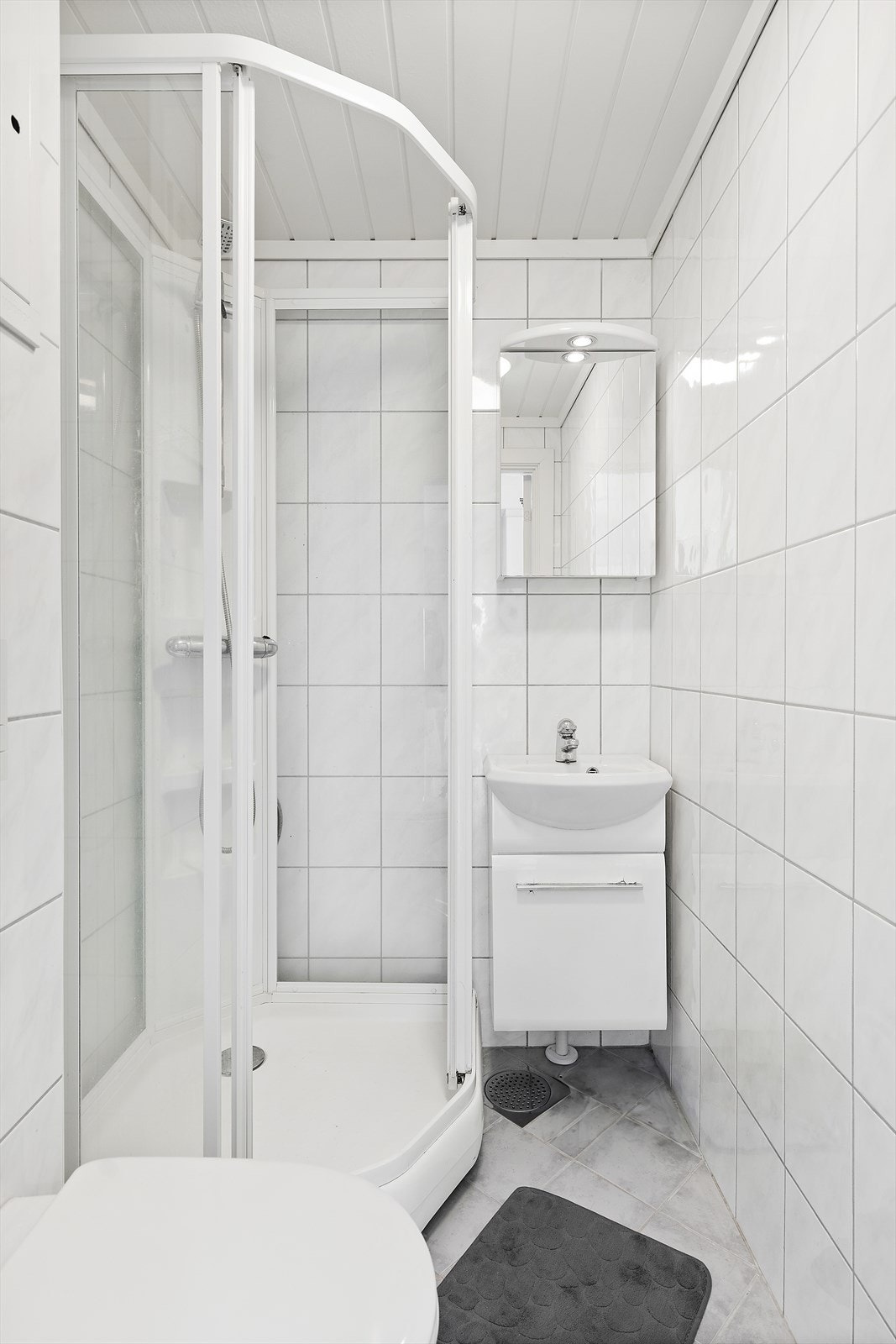 Rommet er innredet med baderomsinnredning med skuff og overliggende servant, samt tilhørende speil. Dusjkabinett og vegghengt toalett. Galleribilde